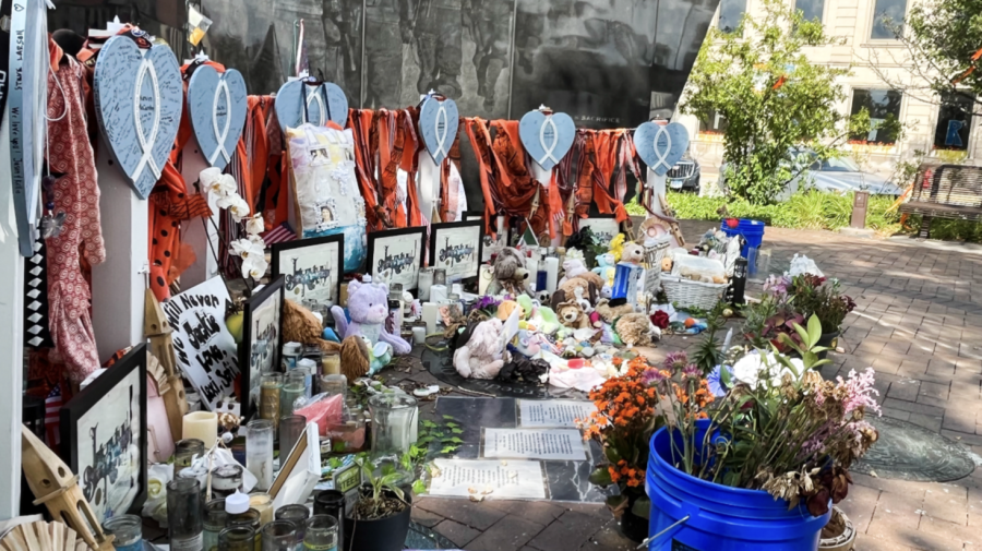 One part of the memorial in Highland Park — set up beneath the Veteran’s memorial — has blue hearts to represent each victim from the July Fourth shooting. Passerbys leave flowers, photographs, stuffed animals and other tributes of remembrance to pay their respects to the victims. (photo by Kevin Lynch)