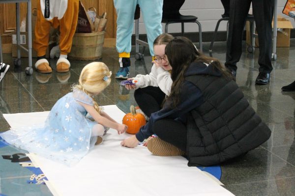 Young girl dressed up as Elsa decorating pumpkins with two volunteers Stella Palm and Mollie Kearns.