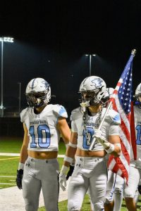 Seniors Lucas Thomas and Parker Ray carry the flag onto the field to begin the game.