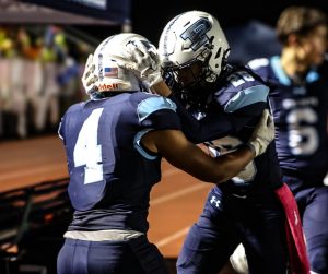 Senior Noah Easter celebrates with teammate on the sidelines. (Photo by Cora Richer)