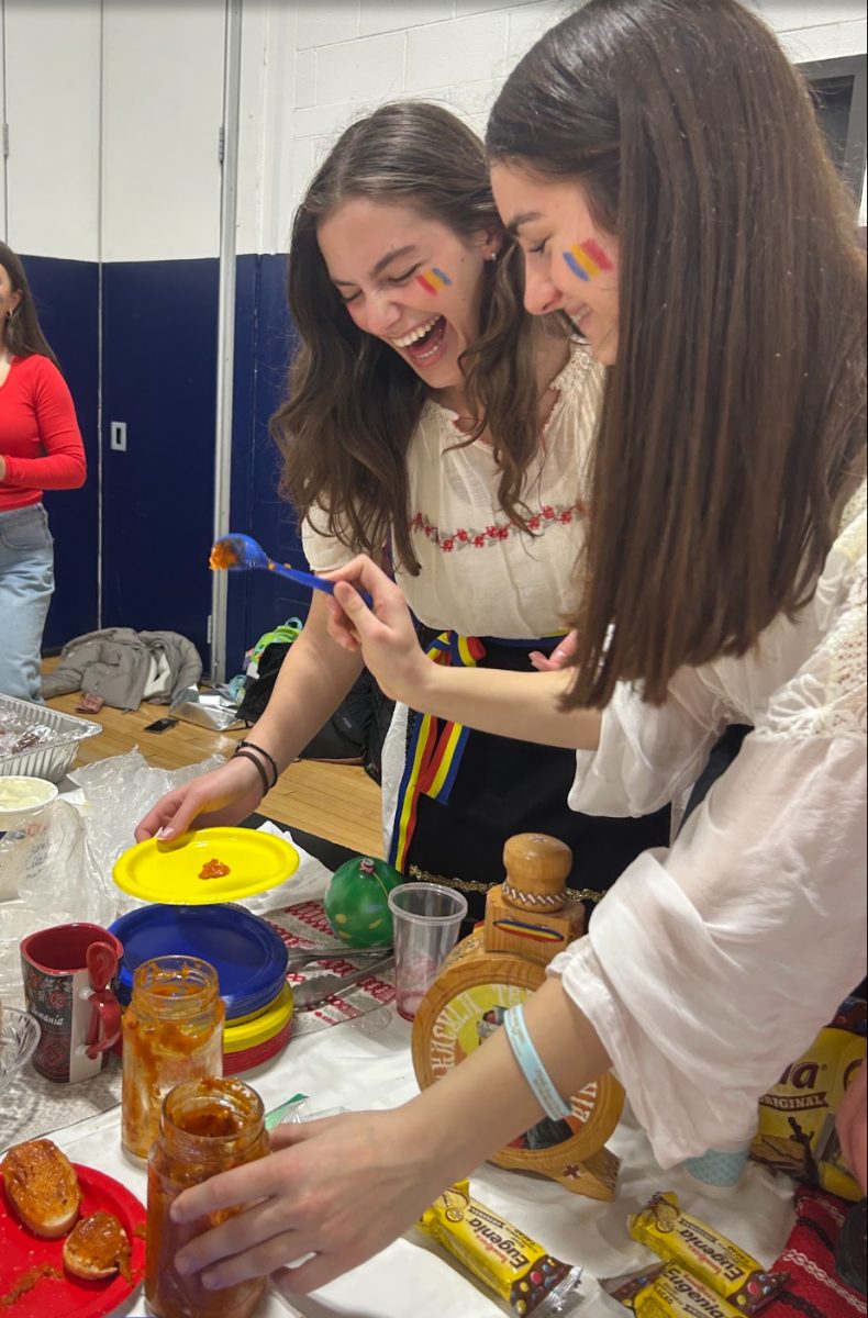 Freshman Selin Pacev puts traditional vegetable spread, zacusca, on a plate, with fellow Romanian senior, Alexis Muntean-Hapa. According to Pacev, the zacusca has been the most popular food item out of the Romanian selection.